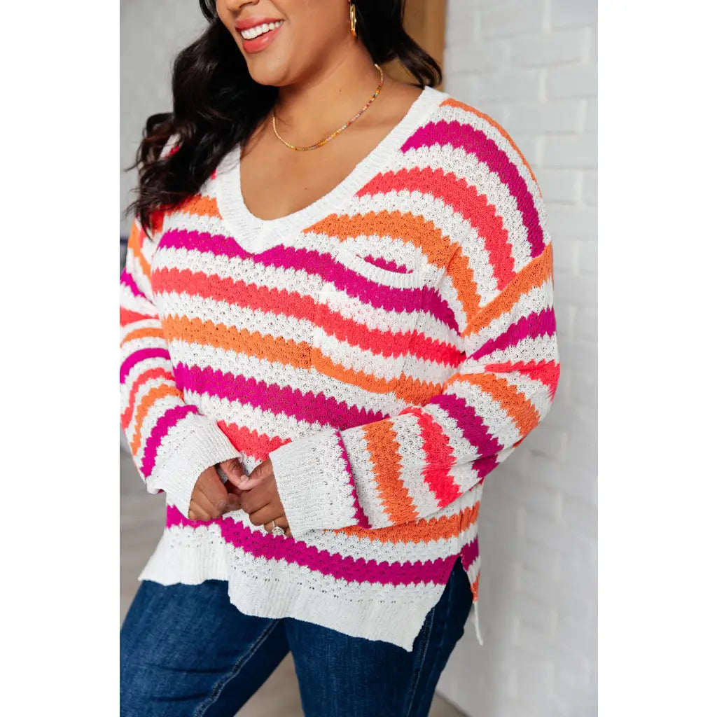 Loose knit striped sweater in coral and magenta. Plus size friendly fit with V-neck side slits. Cozy layering piece