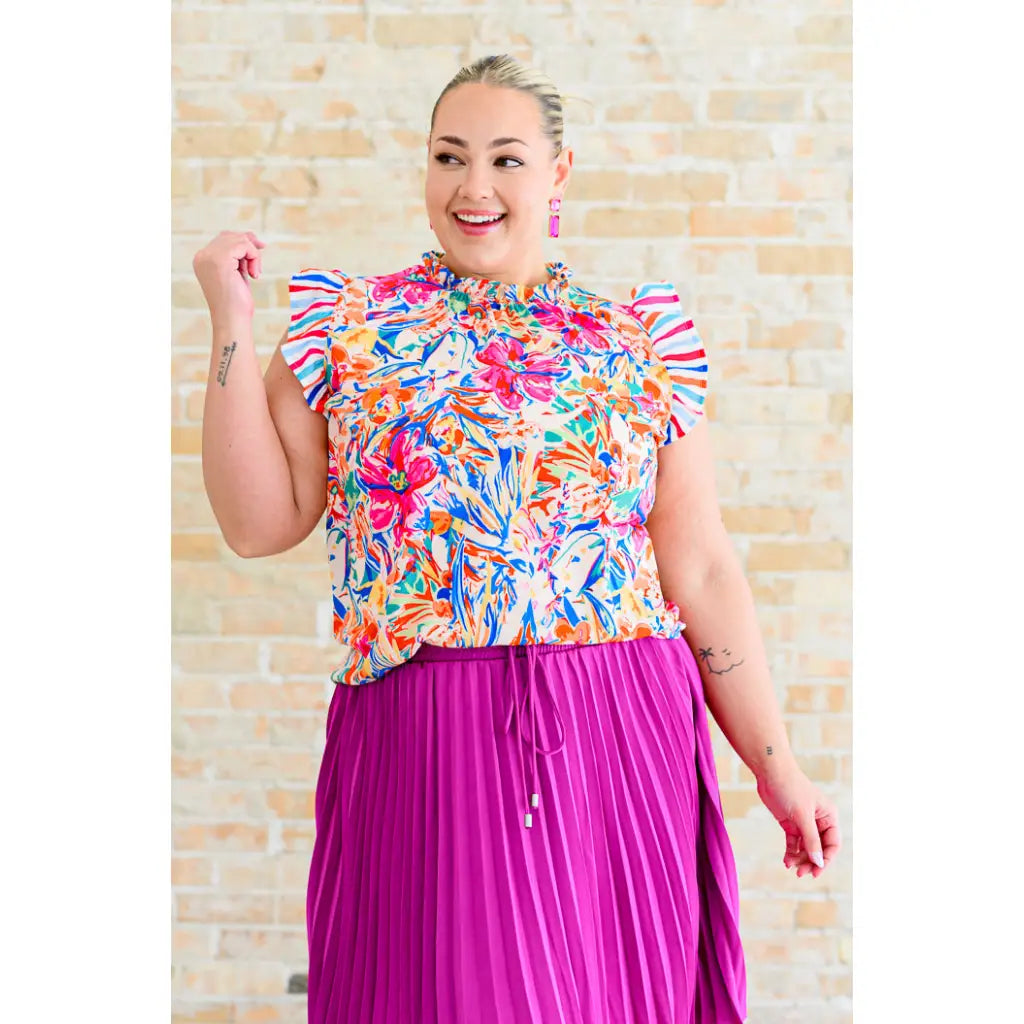 Floral ruffle neck blouse with flutter sleeves and V-keyhole. Polished woven fit offered in sizes SM to 3XL. Ships 2–3