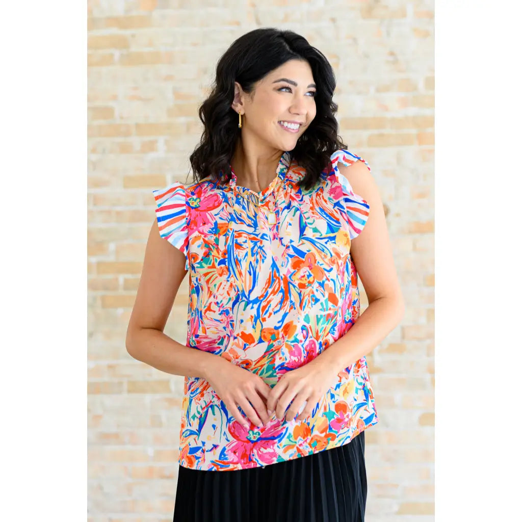 Floral ruffle neck blouse with flutter sleeves and V-keyhole. Polished woven fit offered in sizes SM to 3XL. Ships 2–3