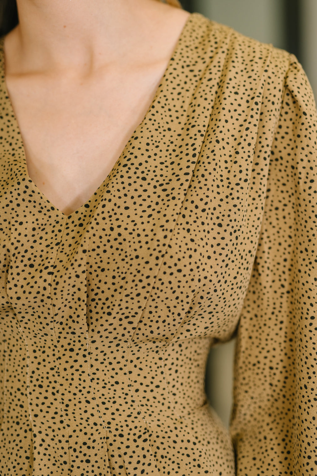 Close-up of a person wearing a beige blouse with black polka dot pattern.