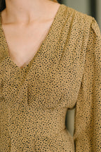 Close-up of a person wearing a beige blouse with black polka dot pattern.