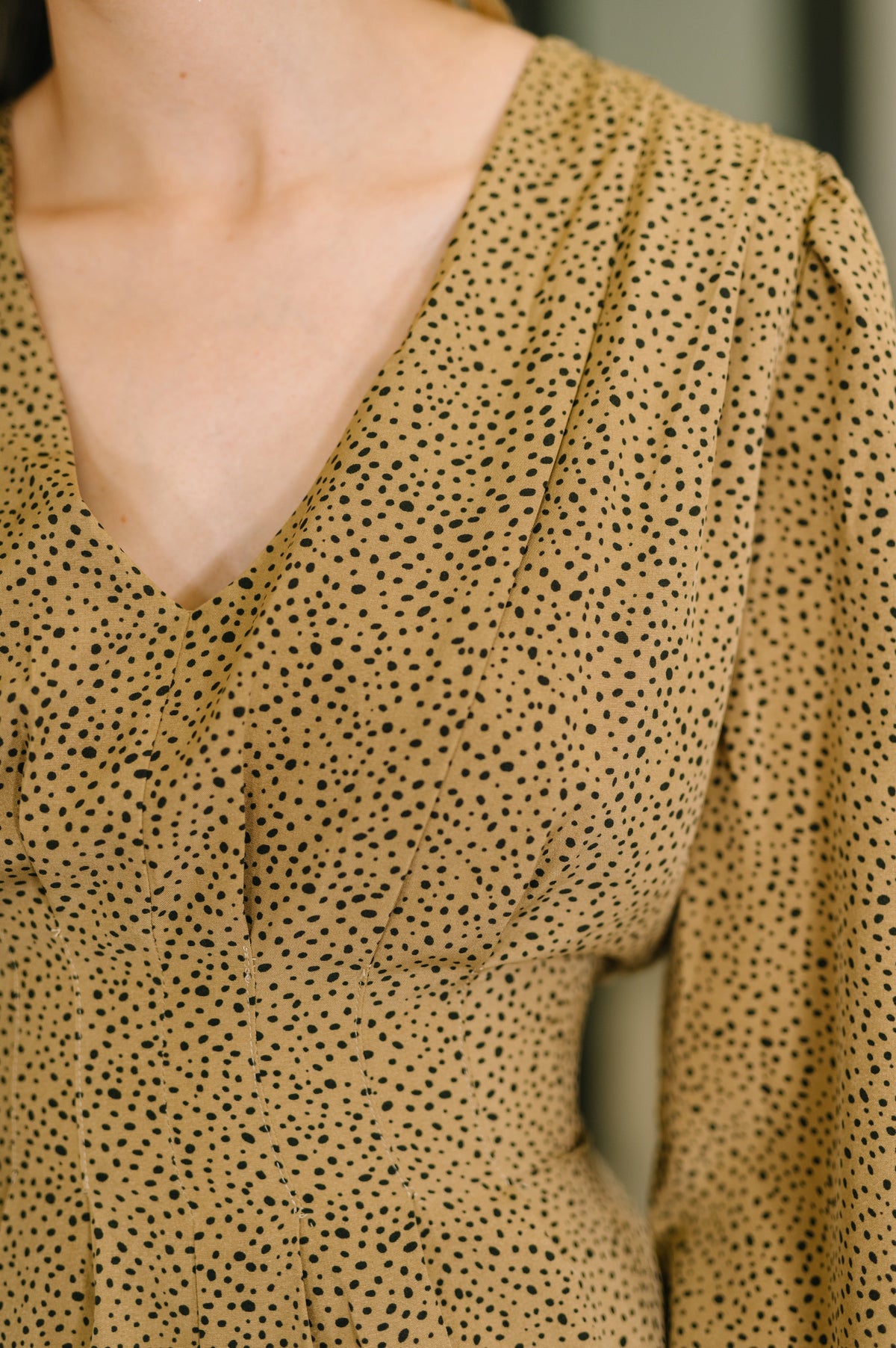 Close-up of a person wearing a beige blouse with black polka dot pattern.