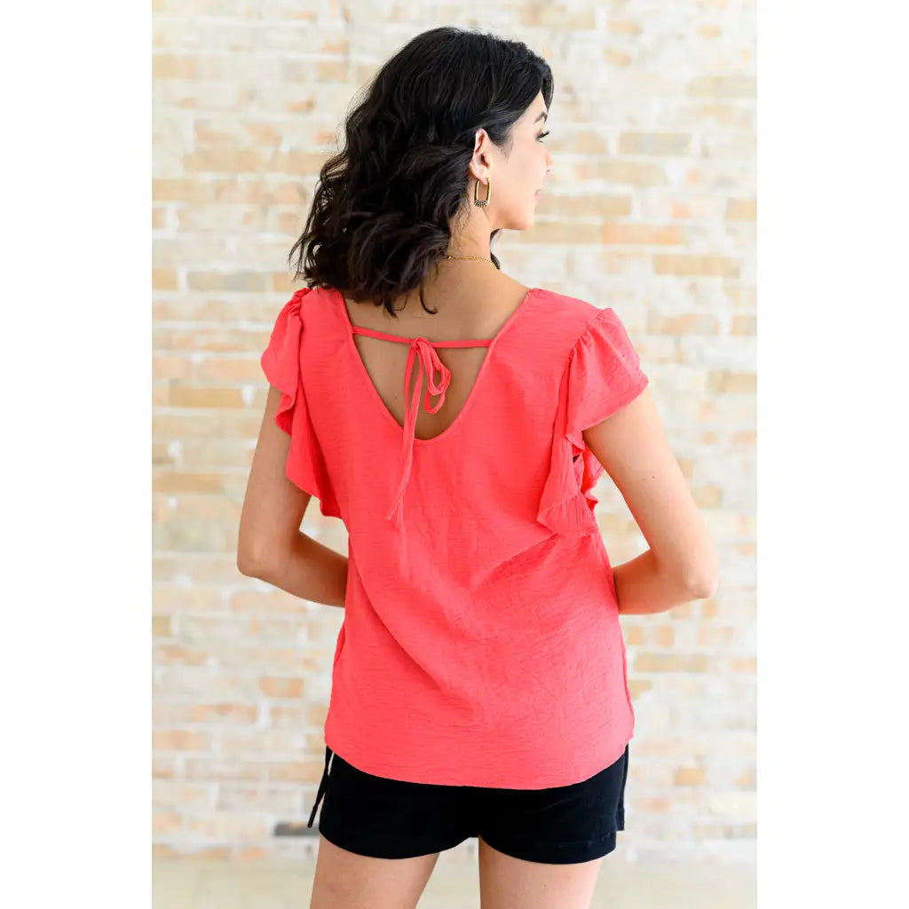 Shop our Coral Pink Ruffle Sleeve Top! Feminine flutter sleeves back tie detail and easy fit for everyday style.