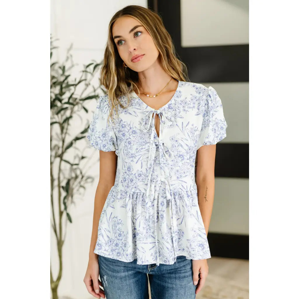 A romantic toile-inspired plus size friendly blouse in ivory and blue with dainty bows a flattering peplum fit. Sweet