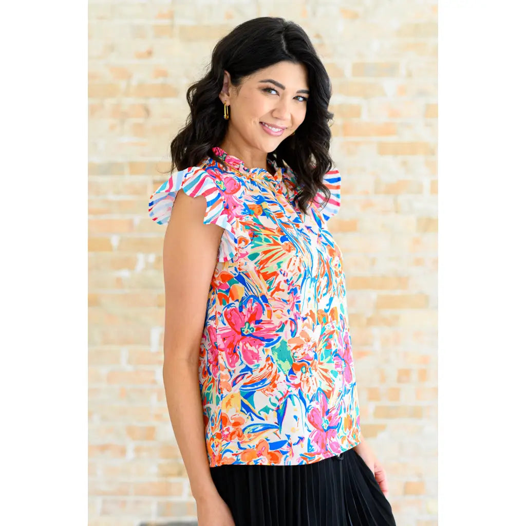 Floral ruffle neck blouse with flutter sleeves and V-keyhole. Polished woven fit offered in sizes SM to 3XL. Ships 2–3