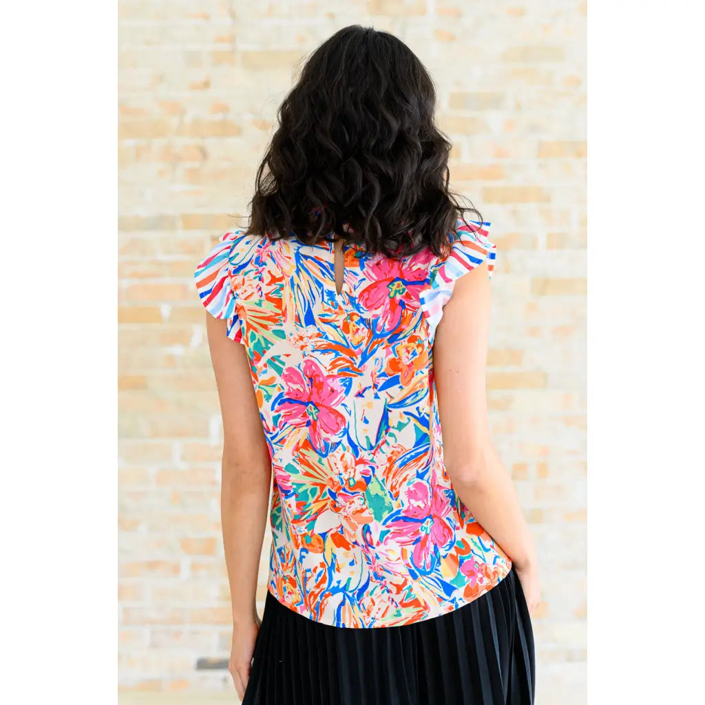 Floral ruffle neck blouse with flutter sleeves and V-keyhole. Polished woven fit offered in sizes SM to 3XL. Ships 2–3